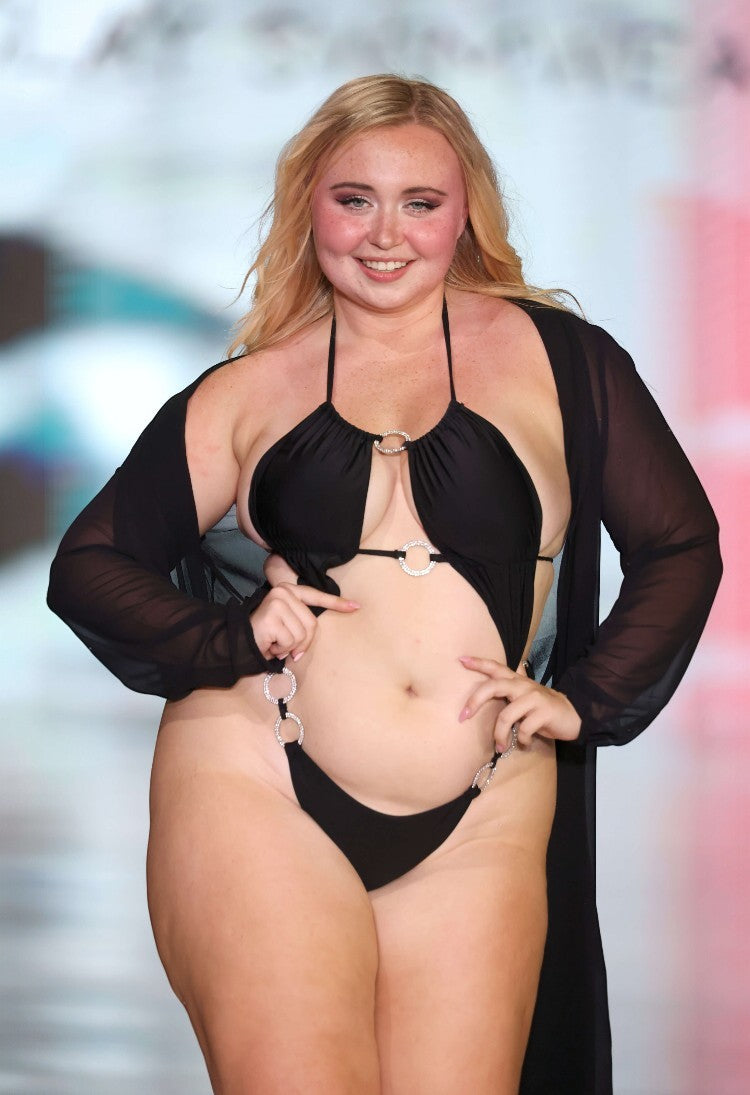 SlaySwimwear black one-piece swimsuit with rhinestone connectors and adjustable straps on a model.