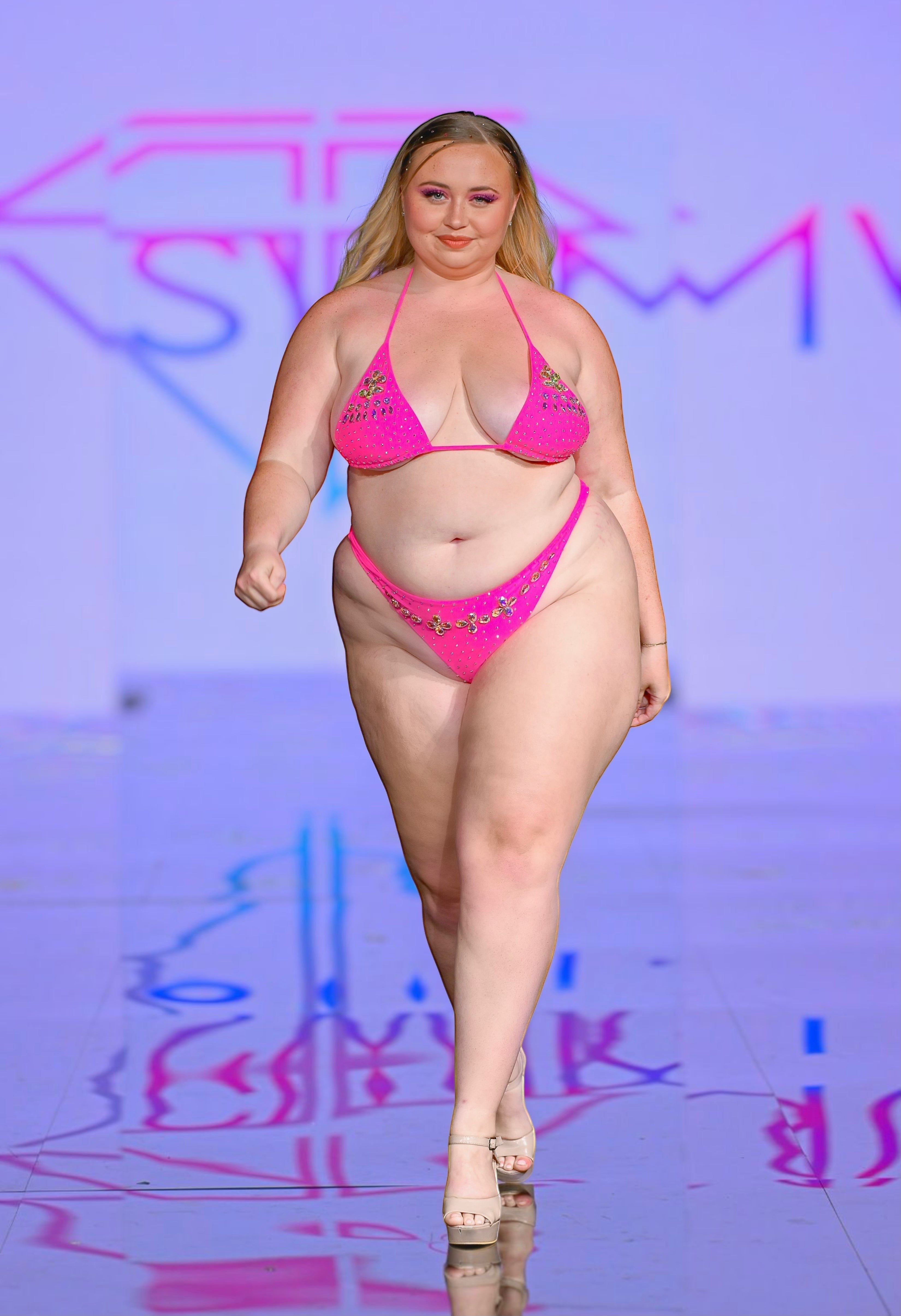 SlaySwimwear hot pink triangle bikini set with rhinestone trim and scrunch back bottom, worn by a model on a runway.