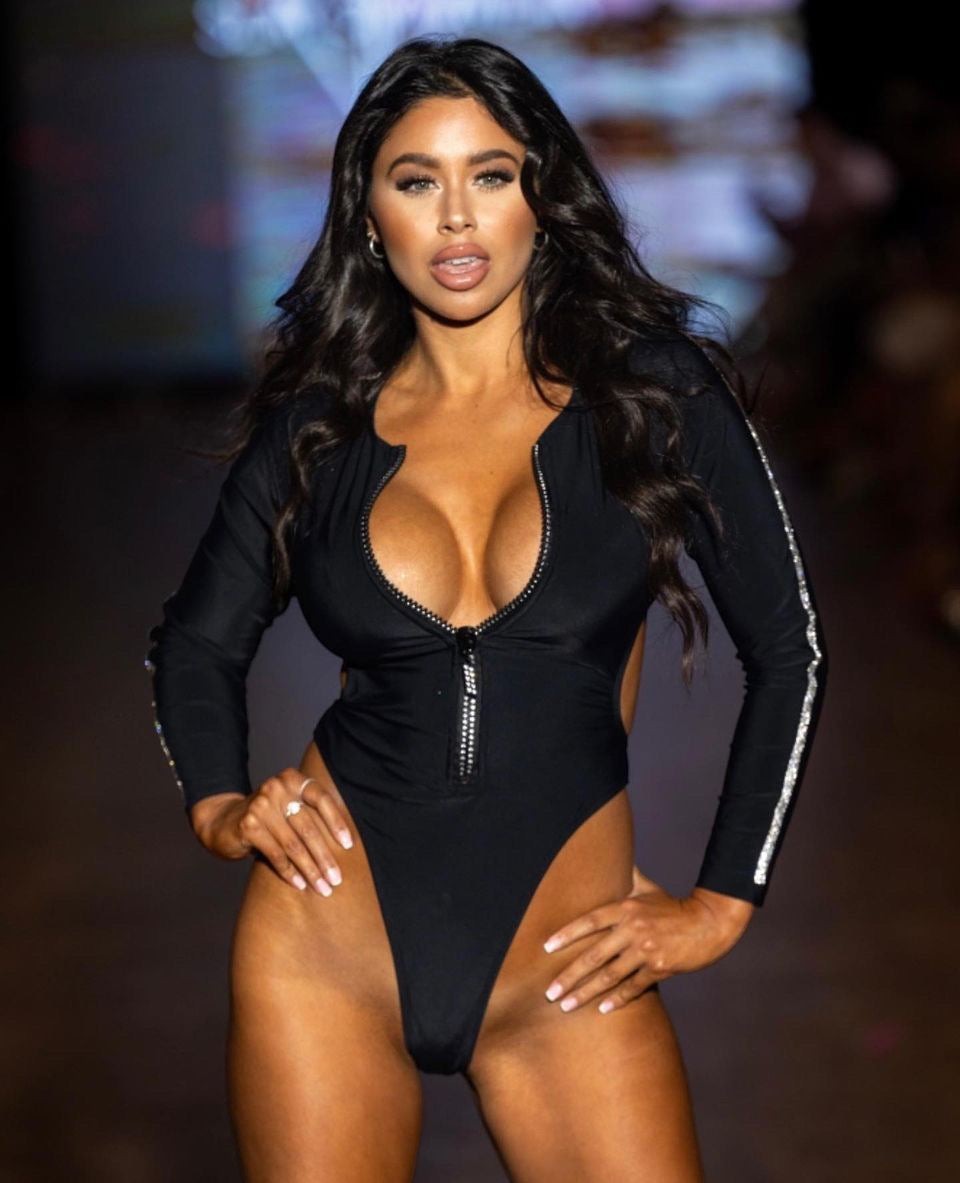 SlaySwimwear black long-sleeve one-piece swimsuit with plunge zip front, side cutouts, and jeweled T-back.