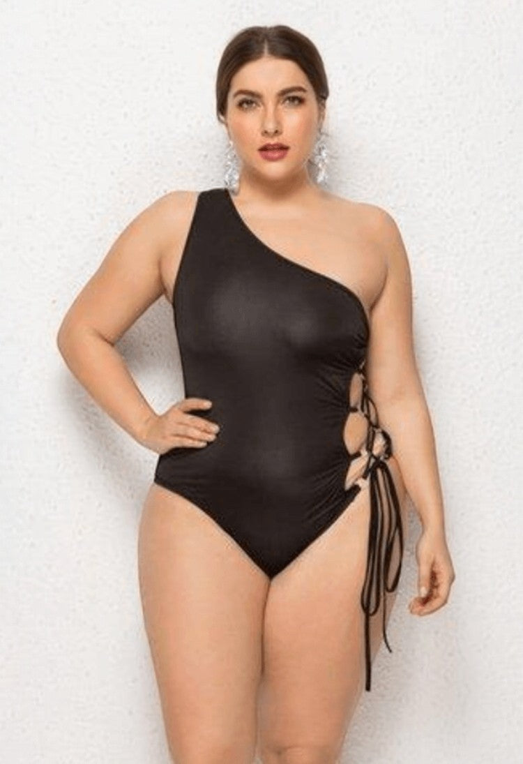 SlaySwimwear black one-shoulder swimsuit with lace-up sides. Model is wearing a size XL.