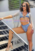 SlaySwimwear blue high-waist bikini set with rhinestone-studded halter top and high-leg bottoms. Model wears a sheer silver cover-up.