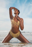 SlaySwimwear gold chain fringe bikini set with underwire top and cheeky bottom, worn by a model on the beach.