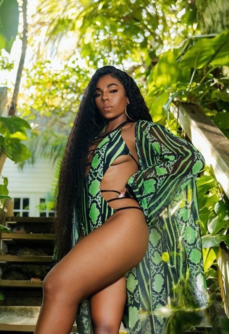 SlaySwimwear green and black snakeskin print one-piece swimsuit with plunge neckline and strappy side cutouts, worn by a model outdoors.