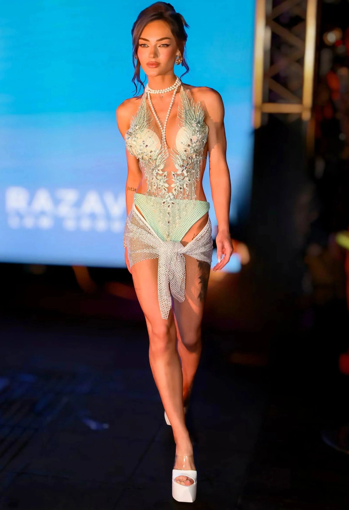 SlaySwimwear Jeweled one-piece swimsuit with pearl and rhinestone embellishments, adjustable halter neck, and sheer mesh skirt.