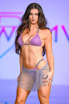 SlaySwimwear purple rhinestone mini skirt with clasp closure and matching bikini top, worn by a model on a runway.